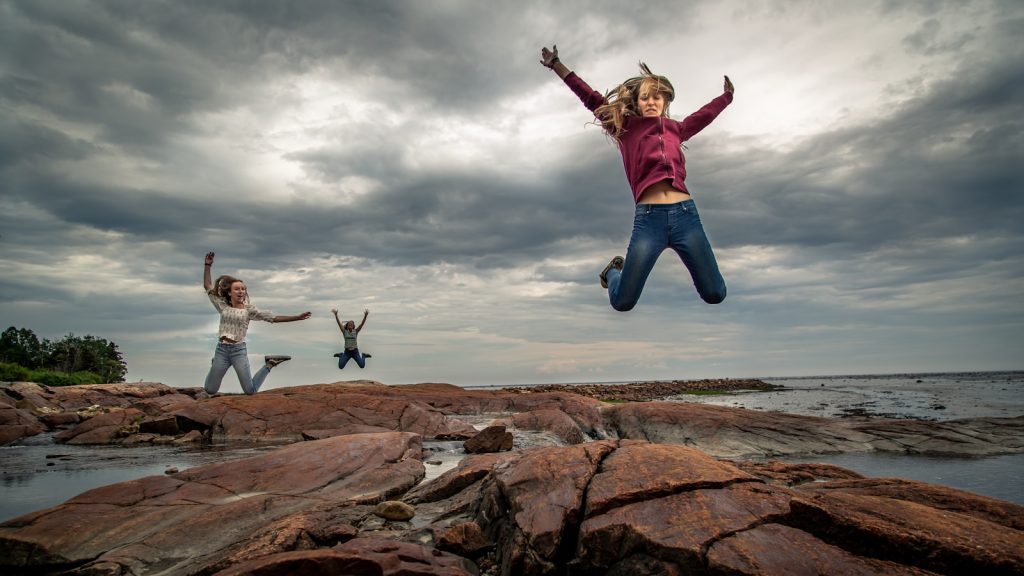 man in red and white jacket jumping on brown rock formation under cloudy sky during daytime